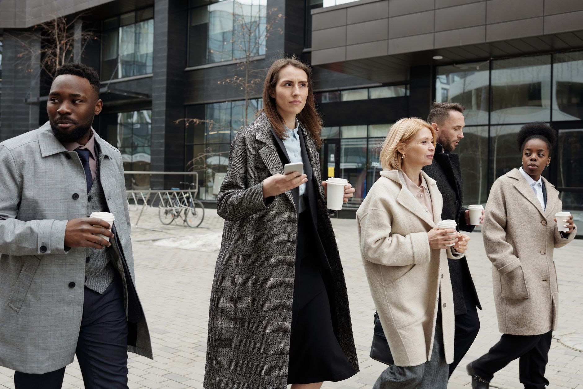 A diverse group of business professionals walking outdoors with coffee in winter attire.