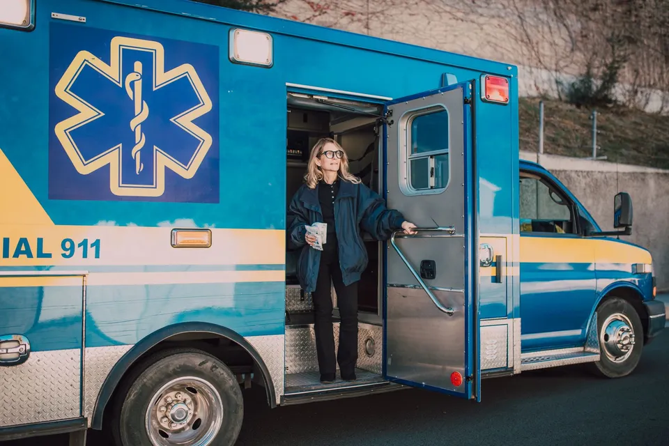 Female paramedic with coffee standing by ambulance during daytime.